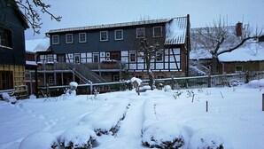 A snow-covered courtyard with a traditional building featuring a gabled roof and a staircase leading to a door. - Holiday apartment with 1 bedroom (Milda, Deutschland)