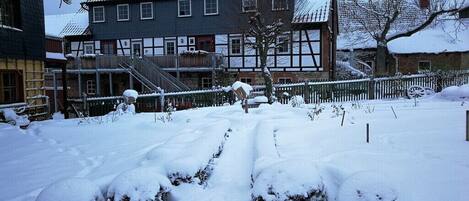 A snow-covered courtyard with a traditional building featuring a gabled roof and a staircase leading to a door.