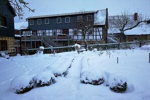 Une cour enneigée avec un bâtiment traditionnel doté d’un toit à pignon et d’un escalier menant à une porte.
