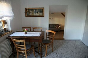 A dining area with a wooden table, four chairs, a vase with flowers, a framed painting on the wall, and a sofa in the background. - Holiday apartment with 1 bedroom (Milda, Deutschland)