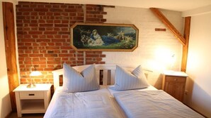 A bedroom with two beds, a nightstand, a wooden headboard, a brick wall, and a framed painting. - Holiday apartment with 1 bedroom (Milda, Deutschland)