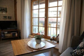 A living room with a wooden coffee table, a television, and a window with curtains. - Holiday apartment with 1 bedroom (Milda, Deutschland)