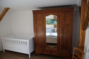 A room with a white crib, a wooden wardrobe with a mirror, and a wooden chair. - Holiday apartment with 1 bedroom (Milda, Deutschland)