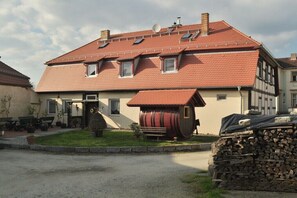 Ein zweistöckiges Gebäude mit rotem Ziegeldach, einem Fass und einem Holzstoß.