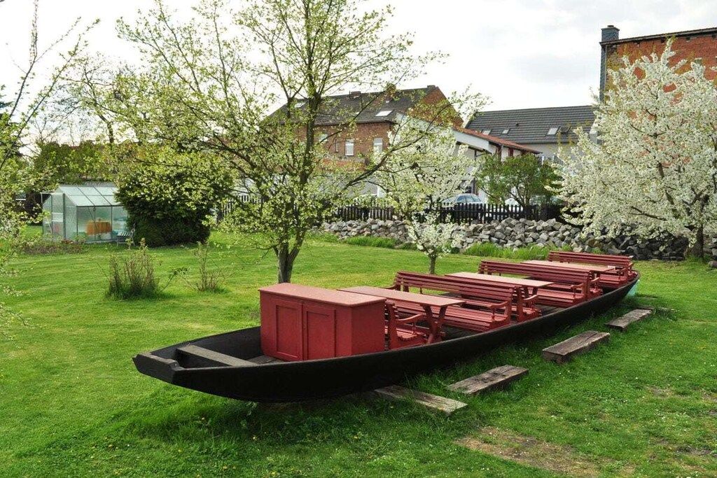 Un espace de détente aménagé en forme de bateau, avec des bancs et une table, entouré de pelouse et d’arbres.