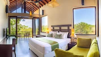 A spacious bedroom with a large bed, a sofa, a desk, and a balcony with a view of greenery.