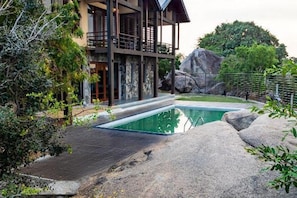 Un edificio moderno de dos pisos con piscina, rodeado de formaciones rocosas naturales y vegetación.