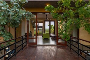 Corredor com piso de madeira e portas de vidro que dão para um quarto com sofá verde e escada.