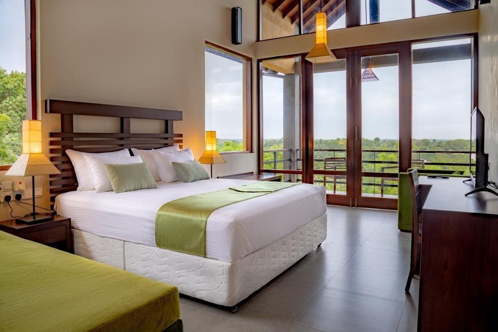 A hotel room with a large bed, a desk, and a balcony with a view.