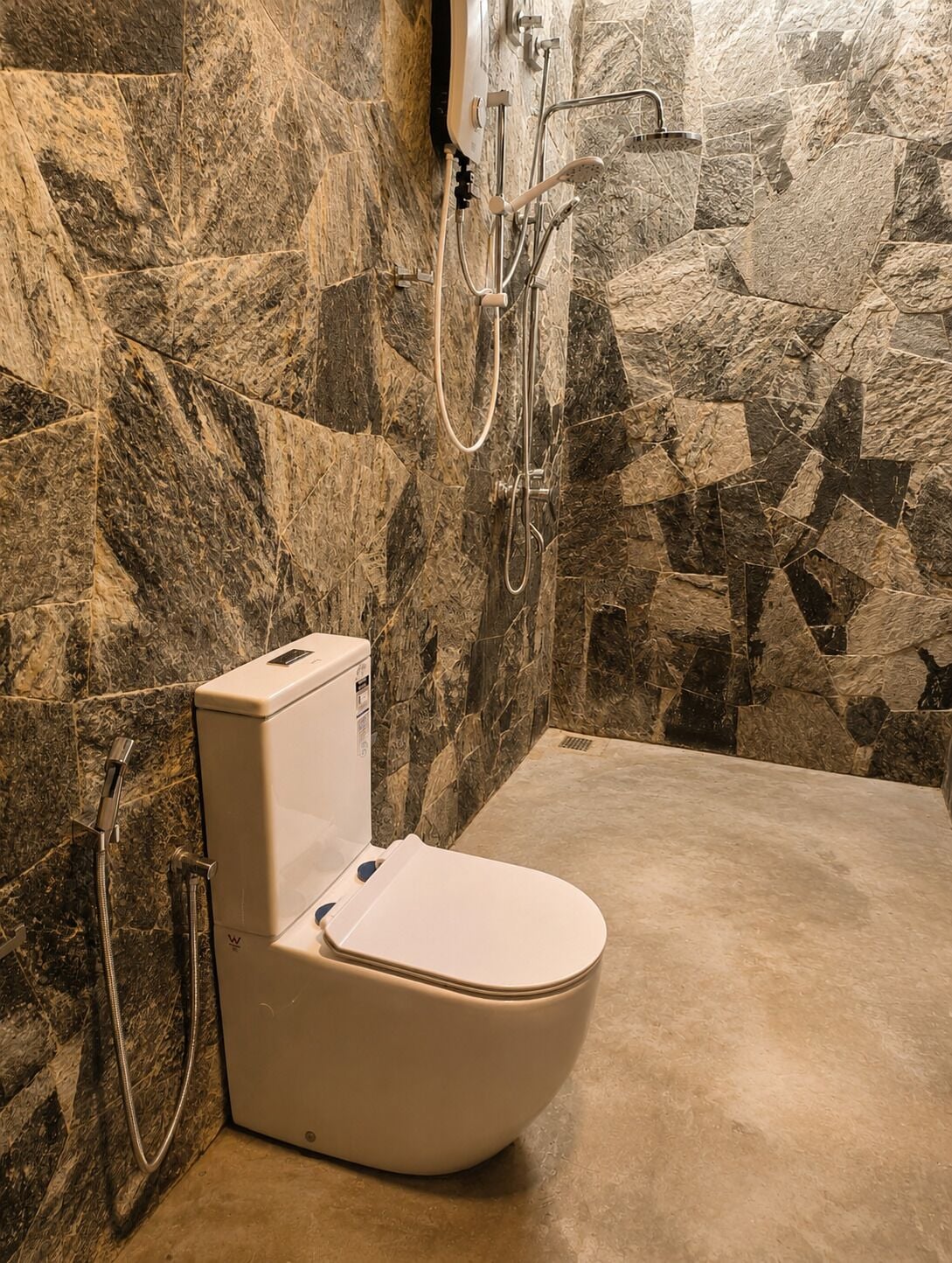 Baño con inodoro, ducha y pared de piedra.
