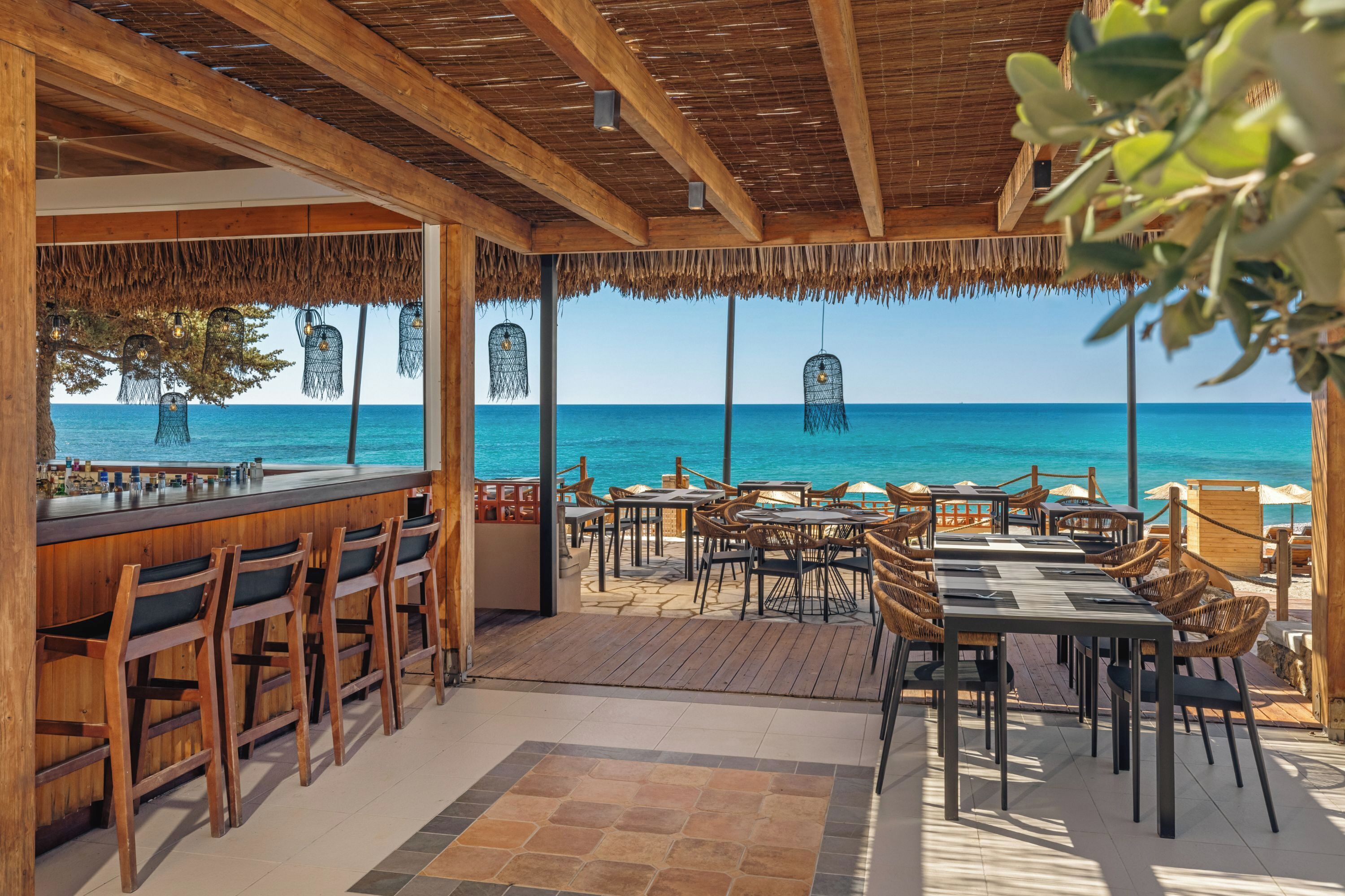 An outdoor seating area with tables and chairs, overlooking a beach.