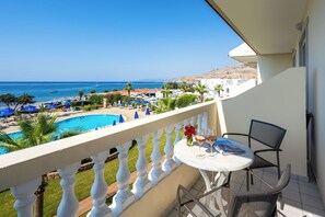 Varanda com vista para uma piscina e praia, uma mesa com dois copos e uma cadeira.