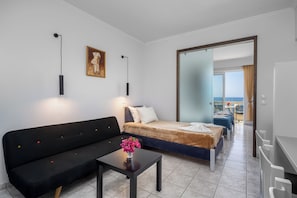 A hotel room with a bed, a sofa, a desk, a mirror, and a view of the sea. - Selia by James Hotel (Lardos)