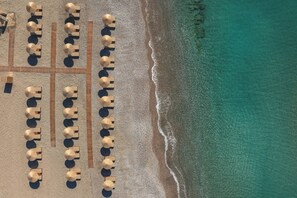 An aerial view of a beach with rows of beach umbrellas and lounge chairs aligned in parallel lines. - Selia by James Hotel (Lardos)