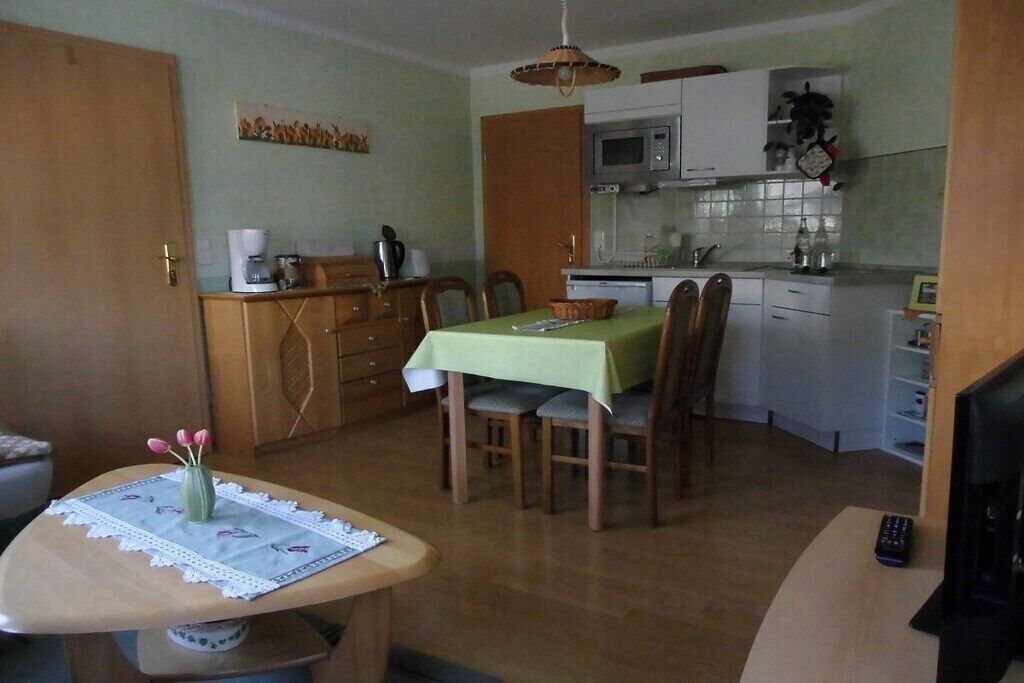 Cocina compacta con microondas, estufa y armarios. Hay una mesa de comedor con sillas y una mesita con un florero.