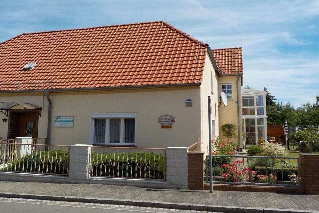 Un bâtiment à deux étages, doté d’un toit recouvert de tuiles rouges, d’un petit porche et d’une enseigne indiquant qu’un commerce est situé au rez-de-chaussée.