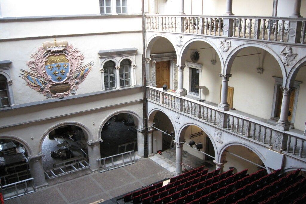 A multi-level building with a balcony, arched windows, and a coat of arms on the wall.