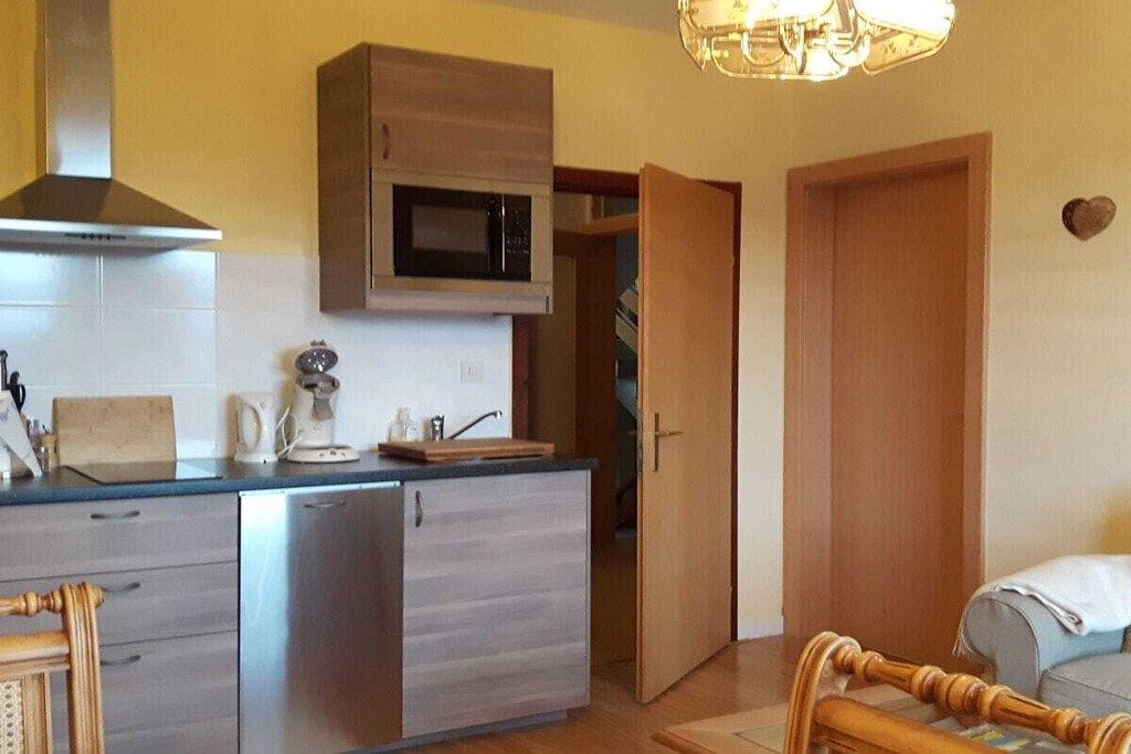 A compact kitchen with a microwave, a coffee maker, and a toaster. There is a wooden cabinet above the counter and a door leading to a hallway.