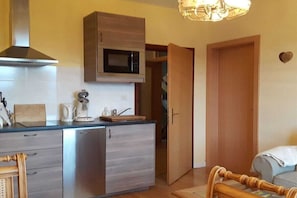 A compact kitchen with a microwave, a coffee maker, and a toaster. There is a wooden cabinet above the counter and a door leading to a hallway. - "Rehsprung" in the Fernblick House (Millstatt)