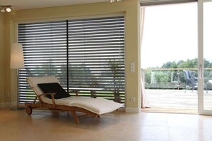 A room with a sun lounger, a lamp, and a view through large windows to an outdoor area with chairs. - Holiday home with 1 bedroom (St.Johann im Saggautal)
