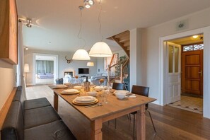 Un espace repas avec une table en bois dressée pour quatre personnes, un banc servant de siège et un escalier menant à un niveau supérieur.