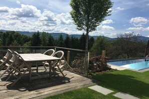 Une terrasse en bois avec une table et des chaises, une piscine et une vue sur les montagnes.