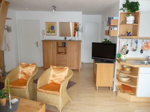 Een knus woongedeelte met een kitchenette, een televisie, rieten meubels en een klein eethoekje.