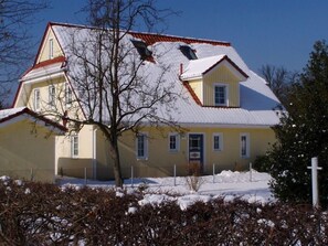 Een huis met twee verdiepingen, een sneeuwbedekte kap en een zichtbare schoorsteen.