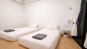Habitación de hotel con dos camas, una mesita y una botella de agua, además de una cortina.