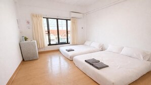 Habitación de hotel con dos camas, una mesita, un ventanal con cortinas y un radiador.