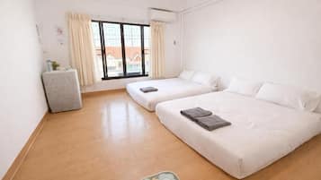 Quarto de hotel com duas camas, uma mesinha, uma janela com cortinas e um radiador.