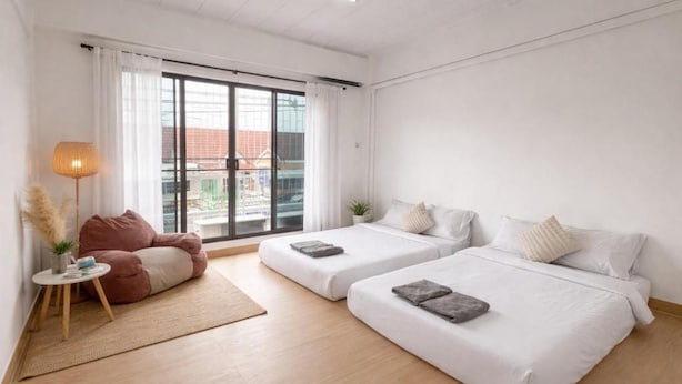 Habitación de hotel con dos camas, un pequeño espacio de descanso y vistas a través de un amplio ventanal.