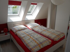 Ein Schlafzimmer mit einem Bett, einem Nachttisch, einer Lampe und einem Fenster mit Blick auf Grünflächen.