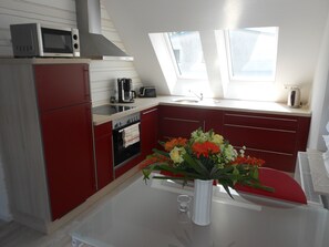Eine kompakte Küche mit Mikrowelle, Toaster und Kaffeemaschine auf der Arbeitsfläche, einem kleinen Backofen und einer Vase mit Blumen auf dem Tisch.