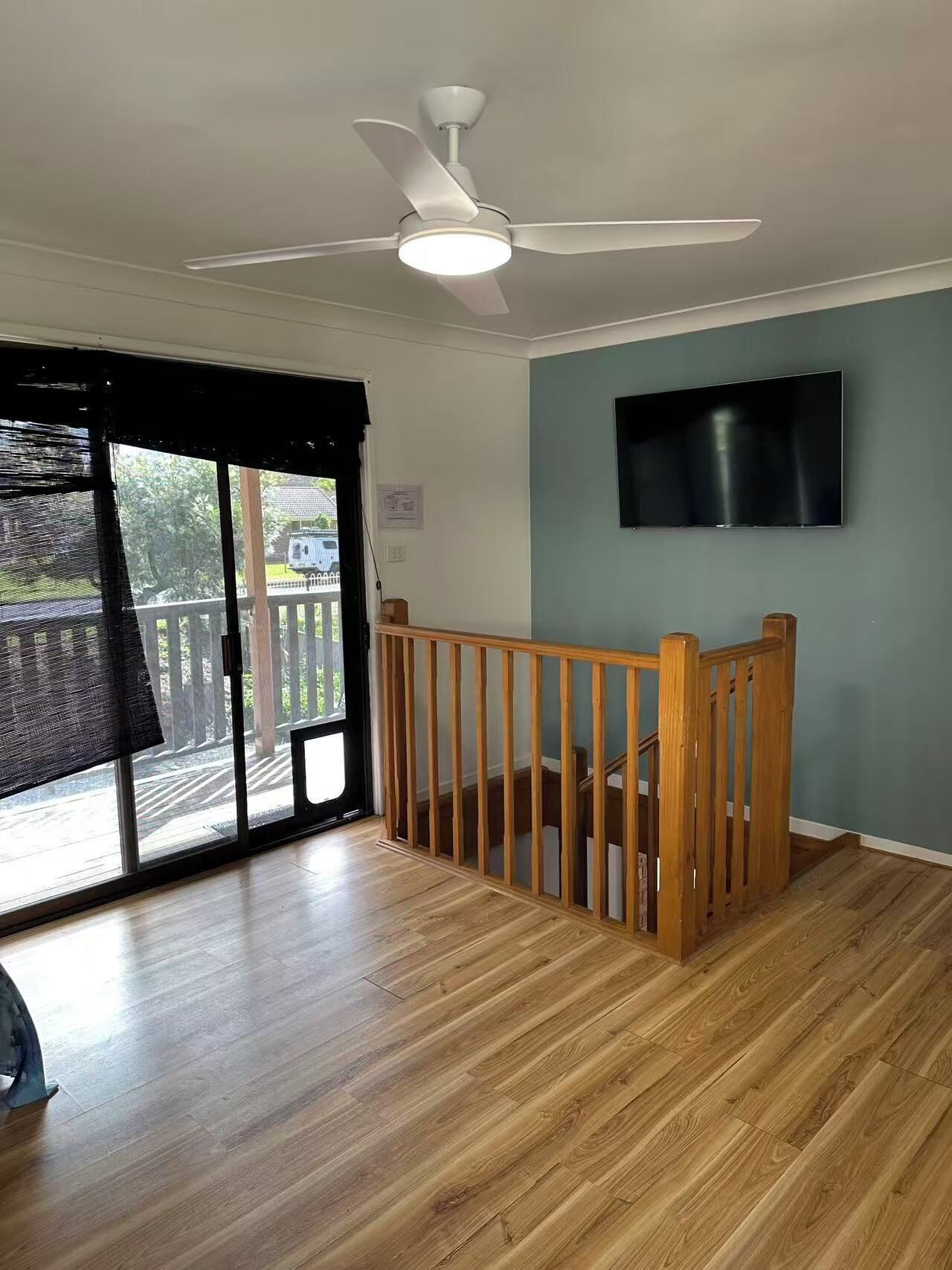 Una habitación con ventilador de techo, televisor montado en la pared y una escalera de madera.