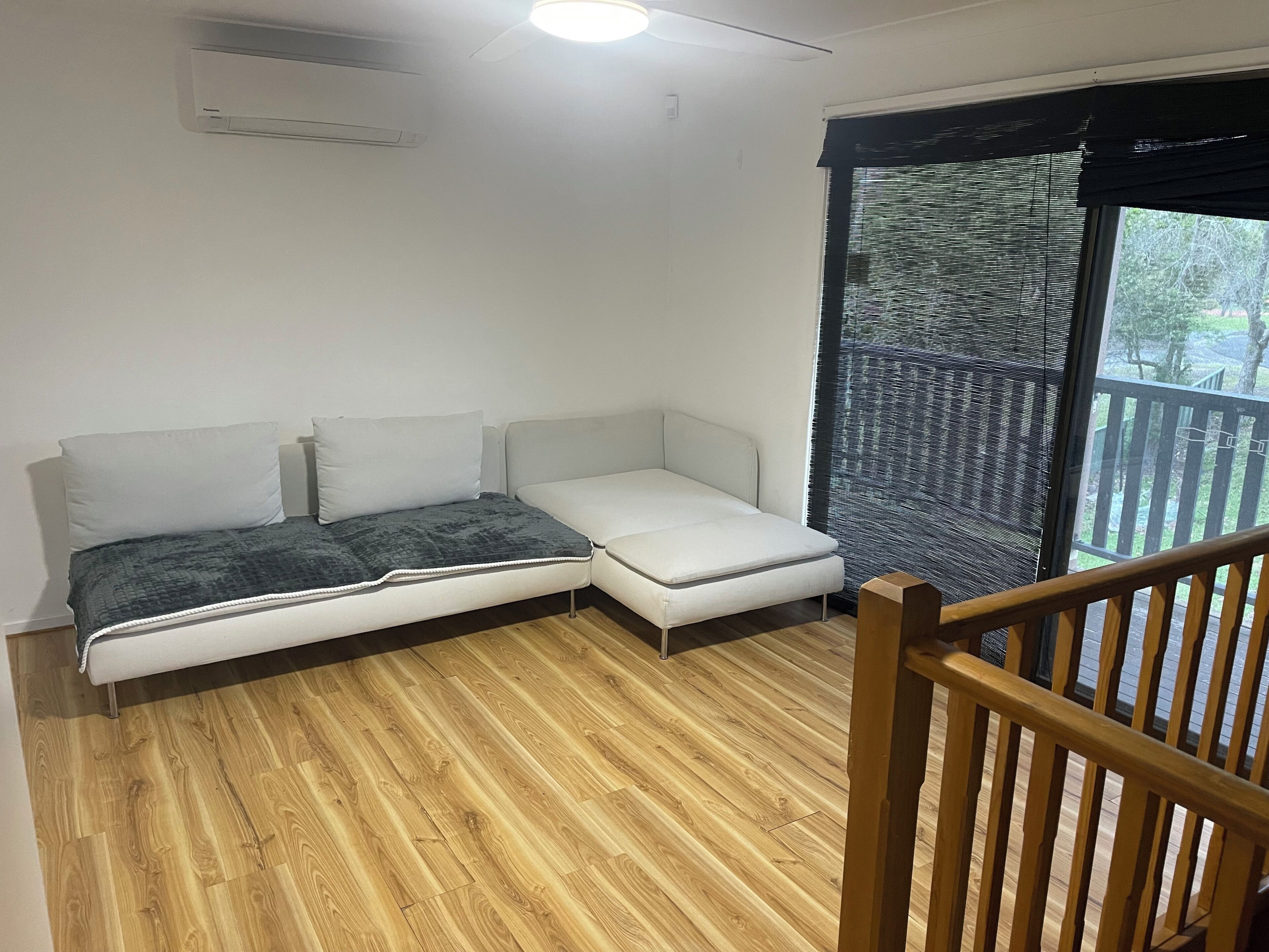 Una habitación con sofá cama, suelo de madera, ventana con vistas y barandilla de balcón.