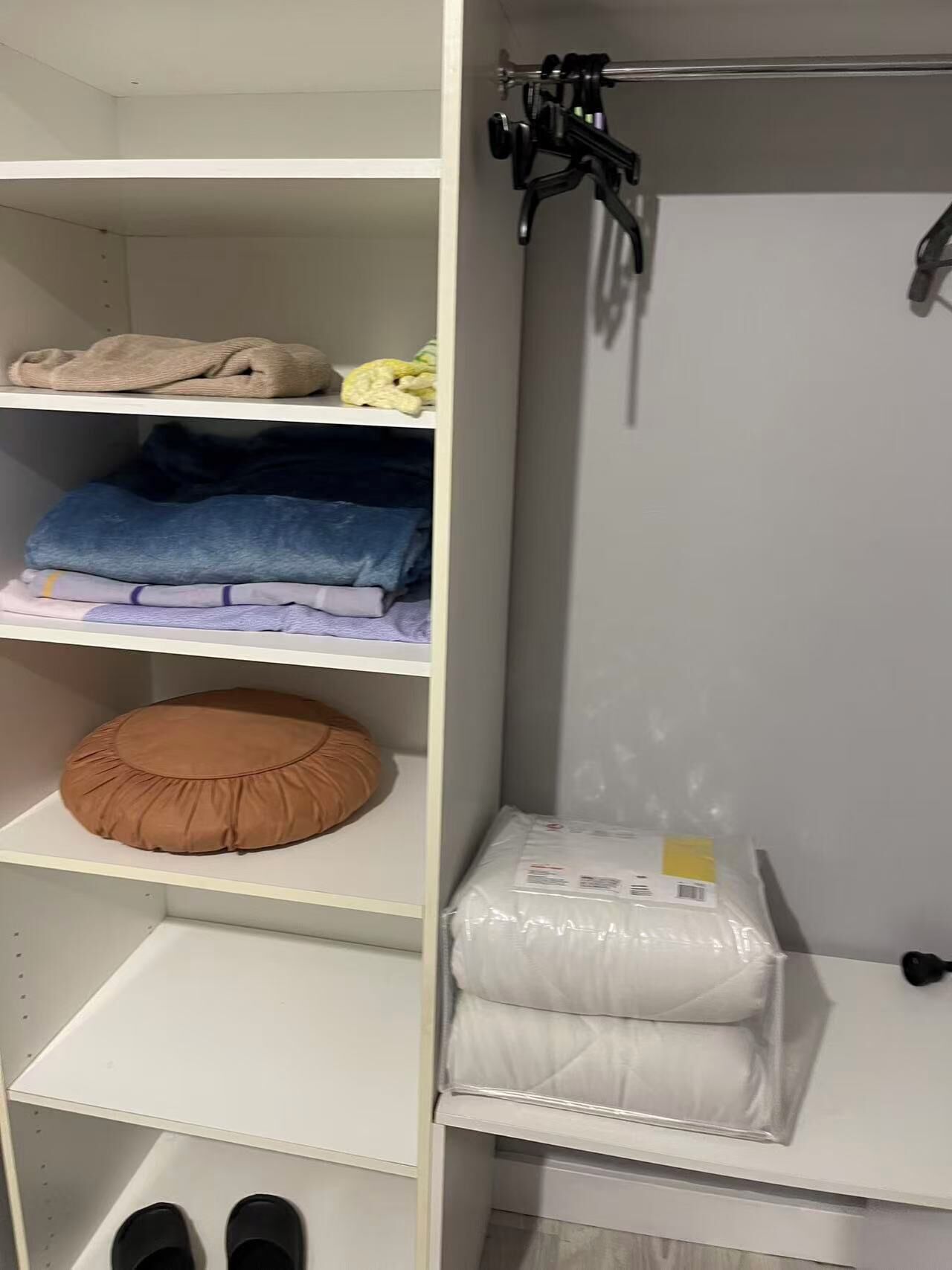 Un armario con repisas que contiene ropa doblada, una percha y un par de zapatos.