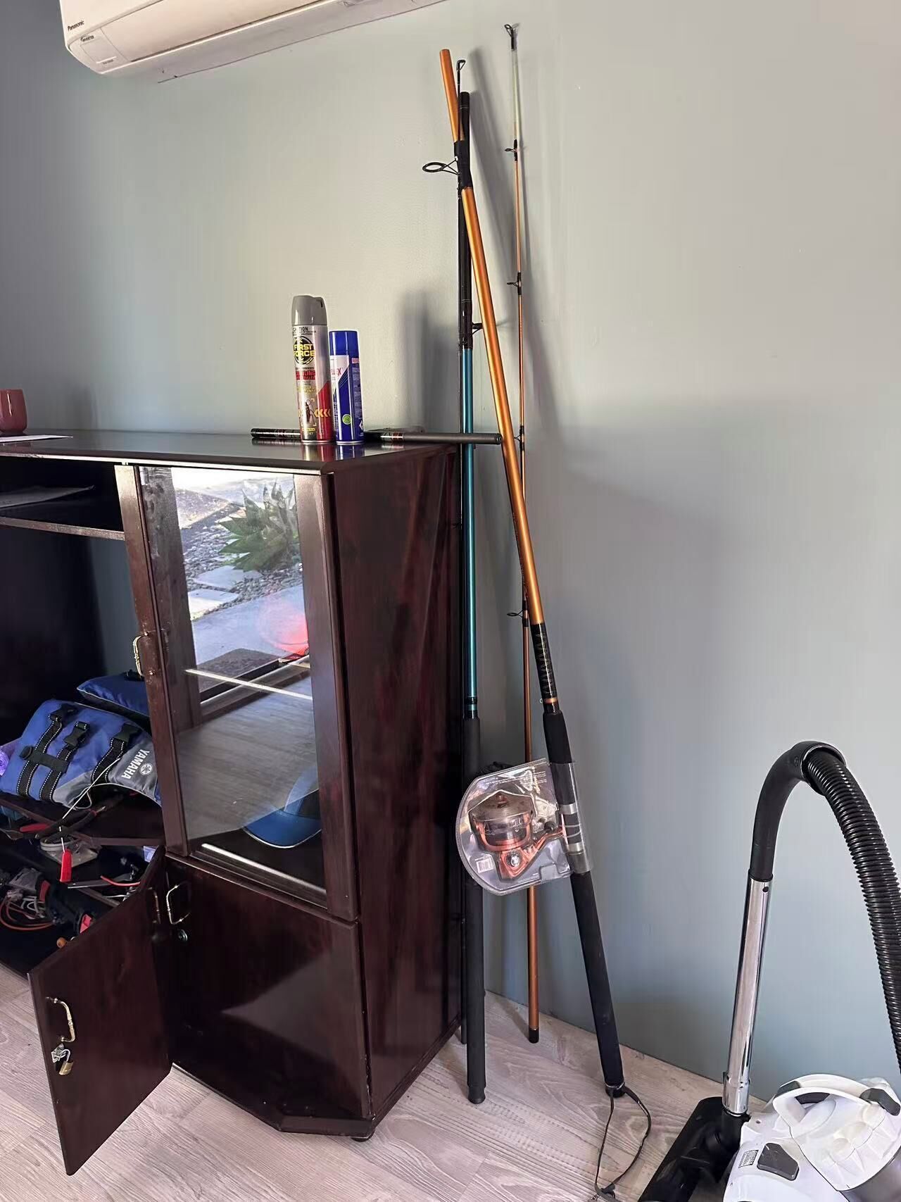 A room with a wooden cabinet, a vacuum cleaner, and fishing rods.