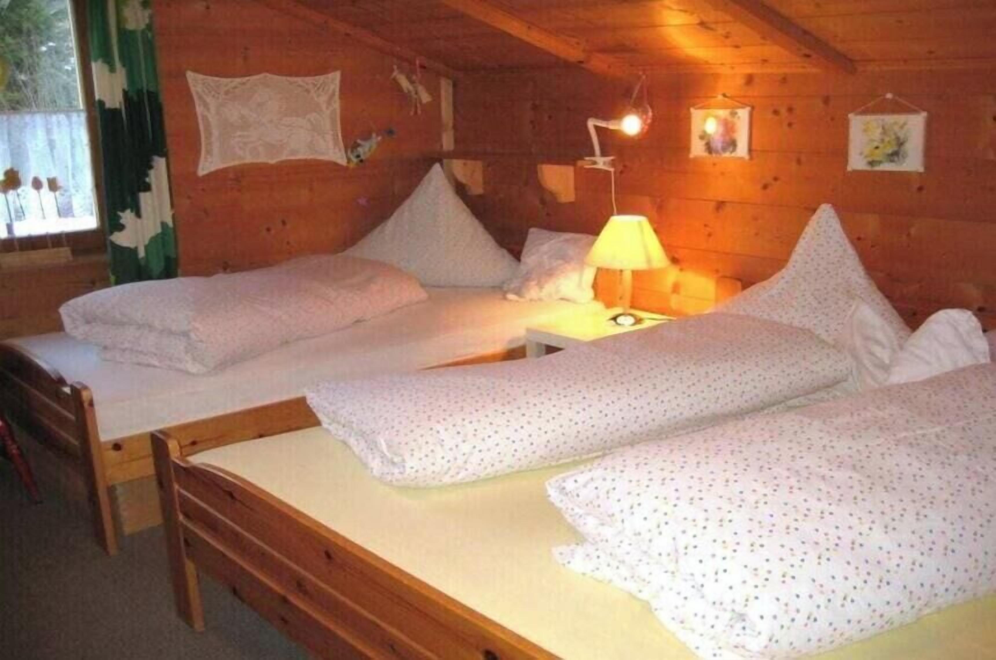Une chambre de style cabane avec deux lits en bois, une table de chevet, une lampe et une fenêtre avec des rideaux.