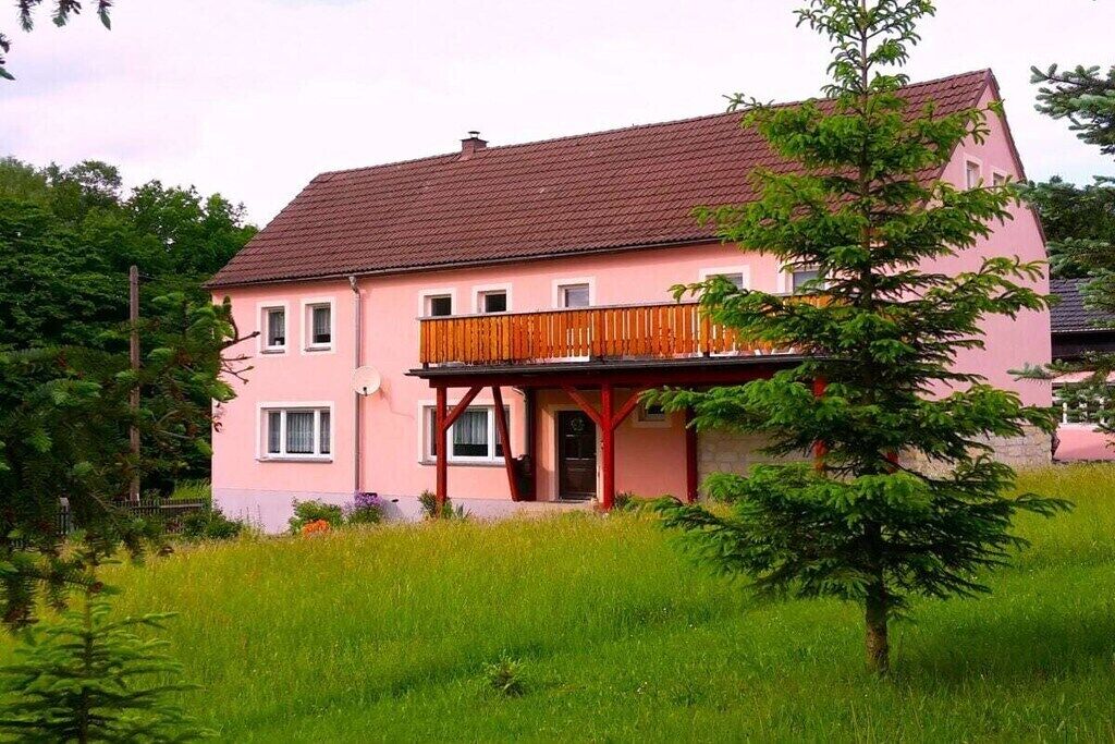 Une maison à deux étages avec un balcon, entourée de verdure.