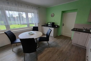 A compact kitchen with a dining table and chairs, a microwave, and a sink. - Holiday apartment with 1 bedroom (Rathmannsdorf)