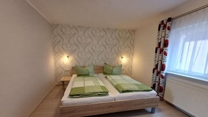 Uma cama de casal com cabeceira, duas mesas de cabeceira e uma janela com cortinas.