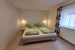 A double bed with a headboard, two bedside tables, and a window with curtains. - Holiday apartment with 1 bedroom (Rathmannsdorf)