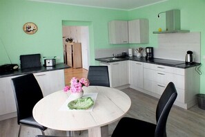 A compact kitchen with white cabinets, a round dining table with chairs, and a small refrigerator. - Holiday apartment with 1 bedroom (Rathmannsdorf)