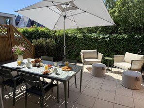 An outdoor patio with a table set for breakfast, a chair, and a sofa. - Vrbo Property (Timmendorfer Strand)