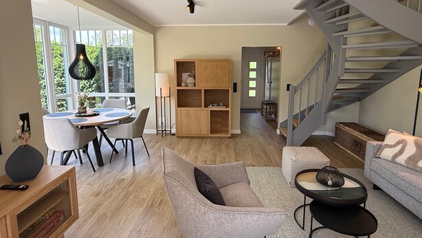 A spacious living area with a dining table, seating, a staircase, and a bookshelf. - Vrbo Property (Timmendorfer Strand)