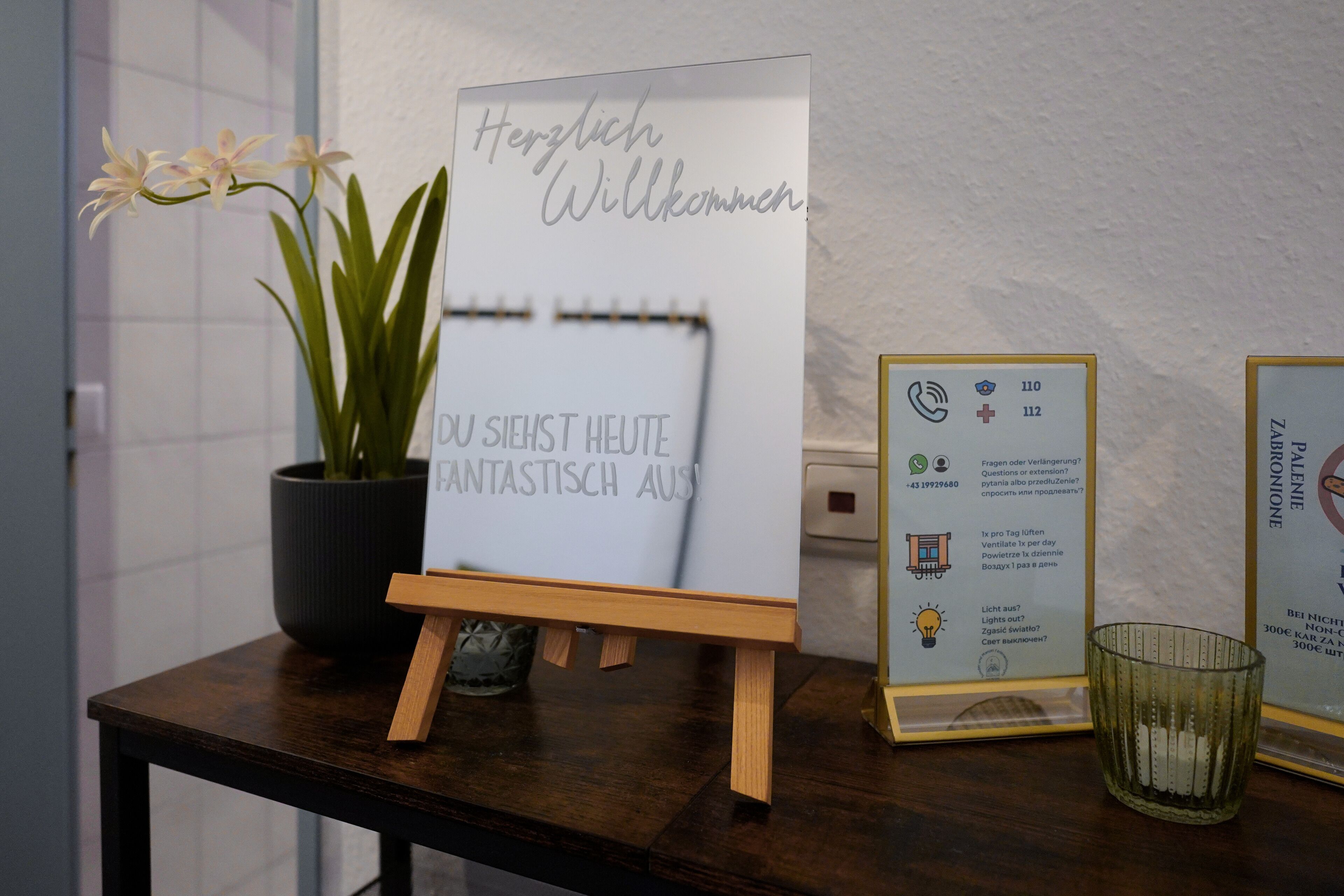 Ein Holztisch mit einem Schild, auf dem 'Herzlich Willkommen' steht, und einem Blumentopf.