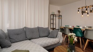 Een moderne woonkamer met een grijze modulaire bank, een ronde salontafel en een eethoek met een houten tafel en stoelen.