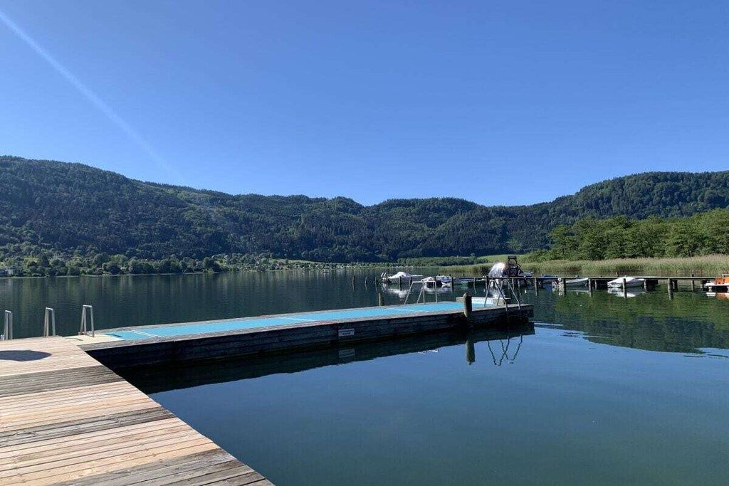 A calm lake with a wooden dock extending into the water, surrounded by forested hills.