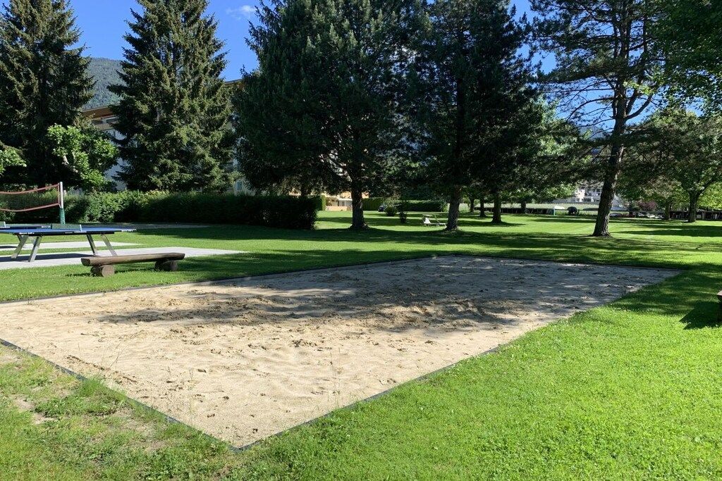 Un parque con un arenero, bancos y árboles.